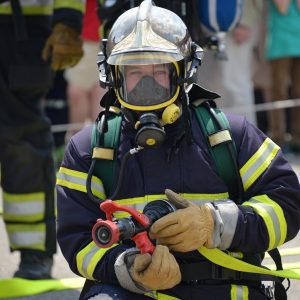 Bombeiro utilizando roupa de aproximação completa com capacete, luvas e máscara em operação.